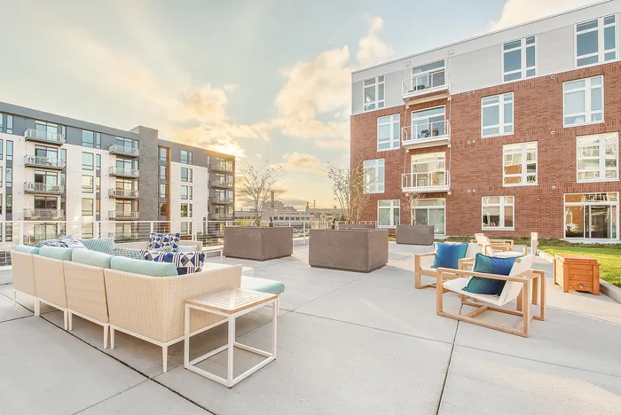 Chic outdoor patio with modern seating overlooking elegant urban apartment complex at sunset.