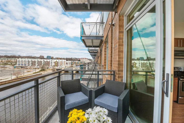 Inviting apartment balcony with cozy chairs and vibrant flowers, offering stunning cityscape and river views.