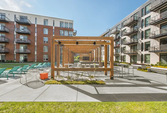 Modern apartment complex with stylish outdoor seating area, featuring sunlit lounge chairs and a sleek pergola, perfect for relaxation and social gatherings.