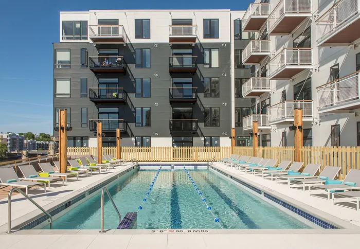 Modern apartment complex with sleek design featuring a refreshing outdoor swimming pool, surrounded by lounge chairs and vibrant balconies.