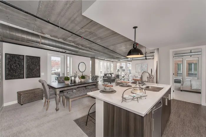 Chic modern apartment interior with open-plan layout featuring a sleek kitchen island, dining area, and cozy living space under industrial-style ceilings.