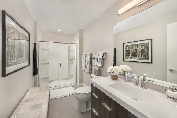 Bright and modern bathroom featuring a sleek glass shower, elegant vanity with fresh flowers, and contemporary decor.