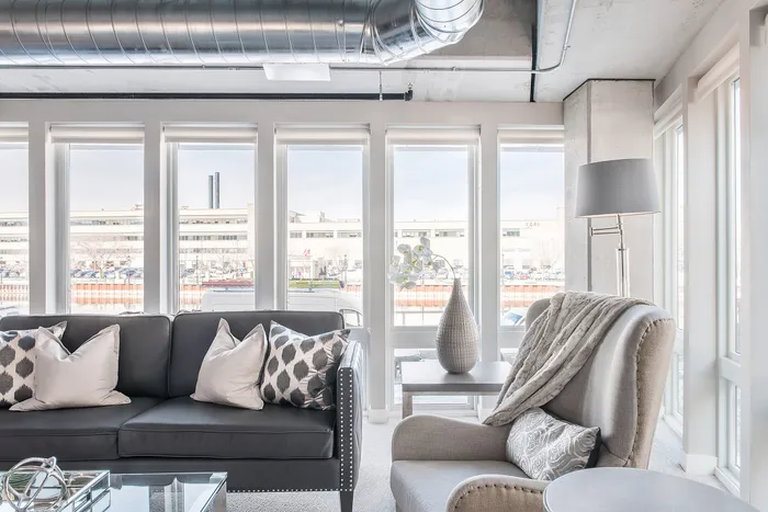 Bright and modern living room with large windows, featuring a sleek black sofa, elegant armchair, and stylish decor.