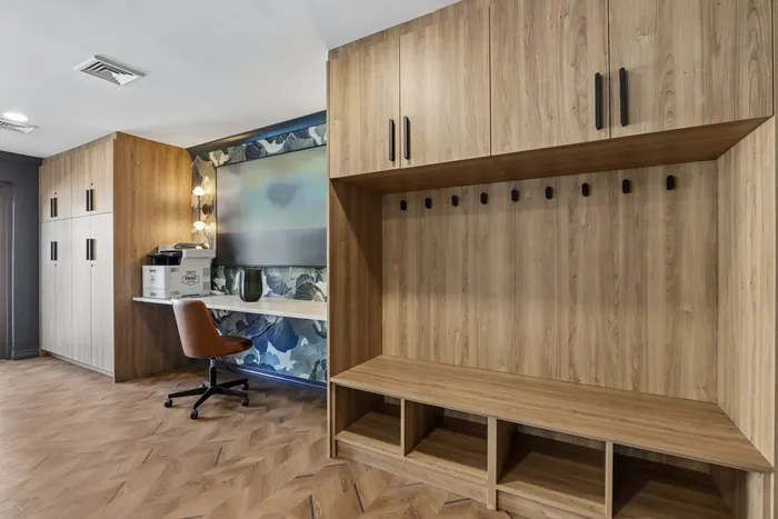 Modern workspace featuring elegant wooden cabinetry, sleek desk, and cozy chair set against a decorative accent wall.