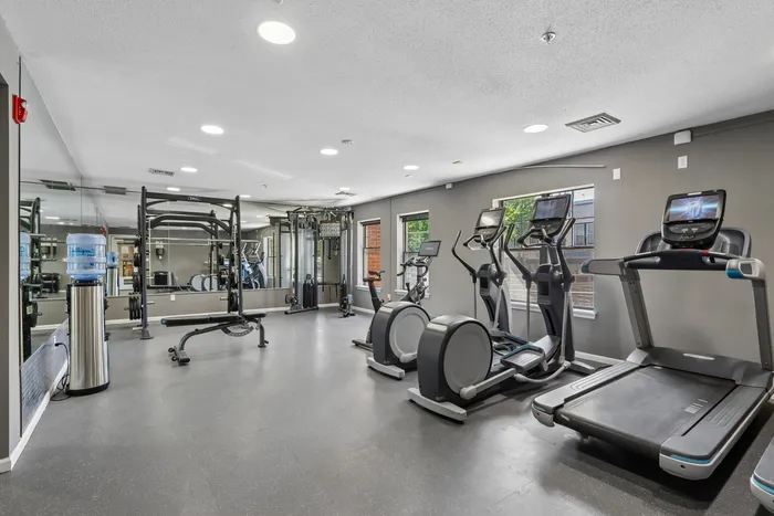Modern fitness center with state-of-the-art equipment including treadmills, ellipticals, and strength training machines in a bright, spacious setting.