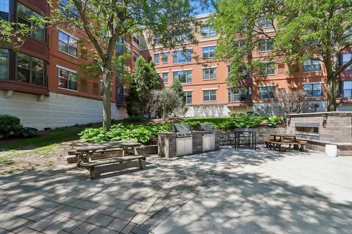 Charming outdoor courtyard featuring lush greenery, barbecue grills, and inviting picnic tables, perfect for relaxing and entertaining.