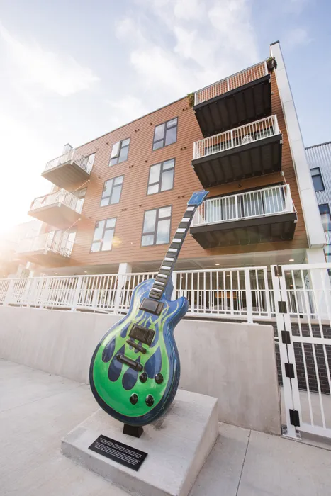 Contemporary apartment building exterior with stylish balconies and a vibrant guitar sculpture, set against a clear sky.