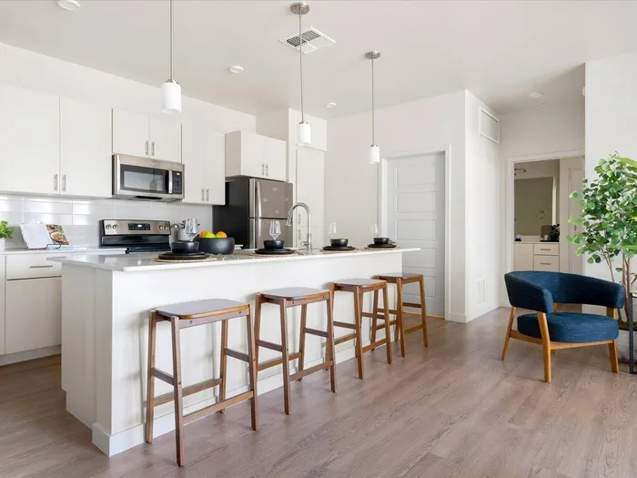 Pet-Friendly Apartments in Glendale AZ - Acero at the Stadium - Modern Kitchen with White Cabinetry, Stainless Steel Appliances, Large Island with Seating, White Countertops, and Hanging Light Set Up