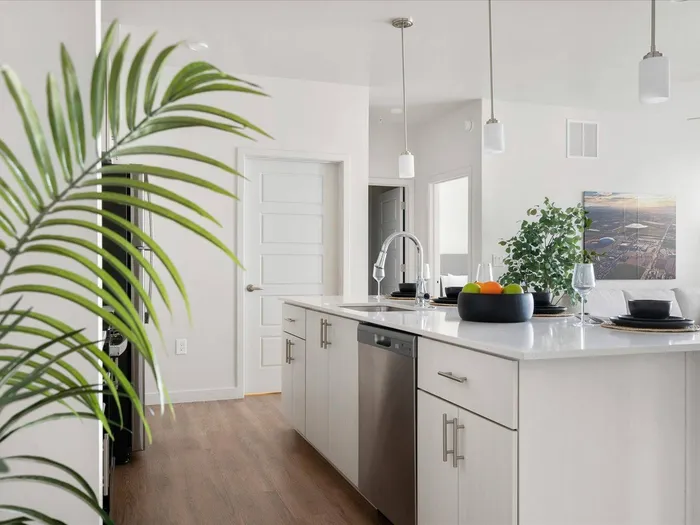 Two-Bedroom Apartments in Glendale, AZ - Acero at the Stadium - Bright White Kitchen With Large Quartz Island, Undermount Sink, Pendant Lights, and Stainless Steel Dishwasher In Open Layout.