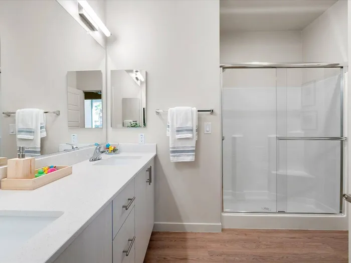 Glendale Apartments - Acero at the Stadium - Bathroom With Vinyl Plank Flooring, Quartz Counters, A Shower, and White Cabinets.