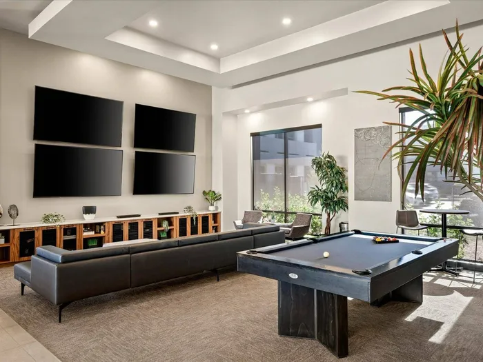 Apartments for Rent in Glendale, AZ - Acero at the Stadium - Indoor Media Center with a Billiards Table, Black Couch, Grey Armchairs, Plants, and Four Mounted TV's