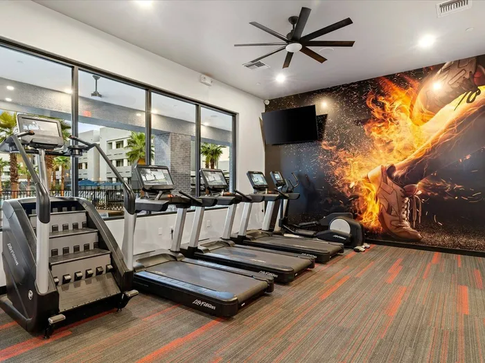 Apartments for Rent in Glendale, AZ - Acero at the Stadium - Fitness Center with Carpeting, Treadmills, an Elliptical, a Ceiling Fan, Large Windows, and a Wall-Mounted TV.