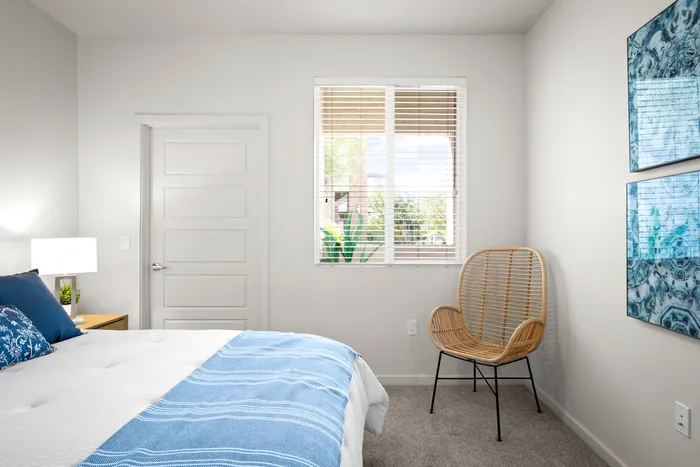 North Phoenix, AZ, Apartments Near HonorHealth Sonoran Crossing Medical Center - Acero North Valley - A Bedroom with a Window, Blinds, a Bedside Table, Wall Art, and an Accent Chair.