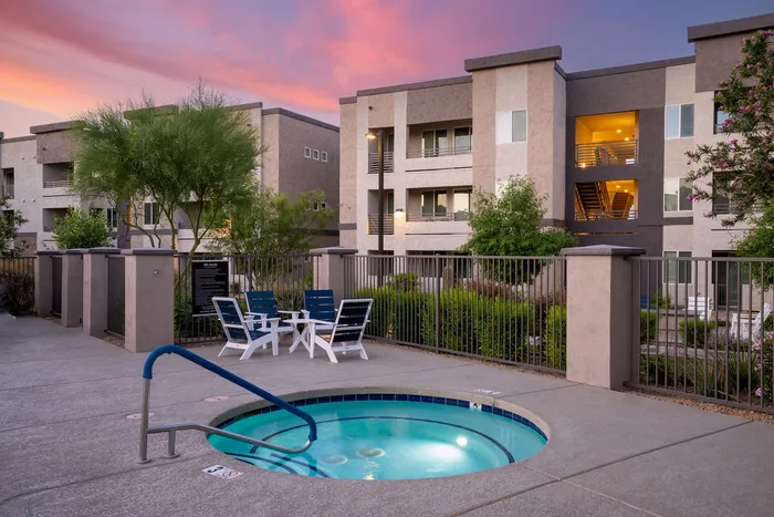 North Phoenix, AZ, Apartments Near United Integrated Services (USA) - Acero North Valley - A Hot Tub with Lounge Chairs, Landscaped Grounds, and Multi-Story Residential Buildings.