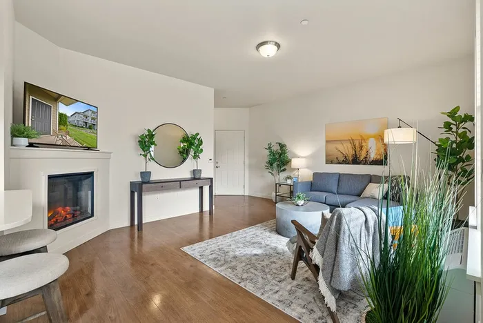 Pet-Friendly Apartments in Ridgefield, WA - Acero Ridgefield - Spacious Living Room With Sofa, Armchair, Coffee Table, Television, Cozy Fireplace, Round Mirror, Wood Floors, and Plants.