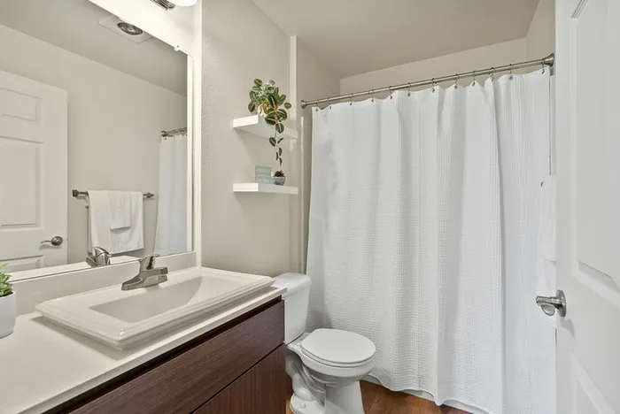 Ridgefield, WA, Apartments - Acero Ridgefield - Bathroom With Wood-Inspired Flooring, A Large Vanity Mirror, A Sink, Wood-Inspired Cabinets, And A Shower With Tub.