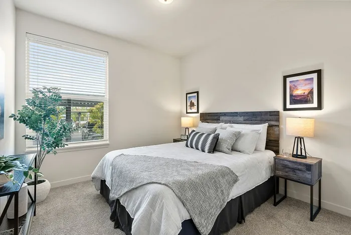Ridgefield, WA, Apartments With In-Unit Washer and Dryer - Acero Ridgefield - Bright Bedroom With Wood Headboard Bed, Neutral Bedding, Nightstands With Lamps, and Large Window With White Blinds.