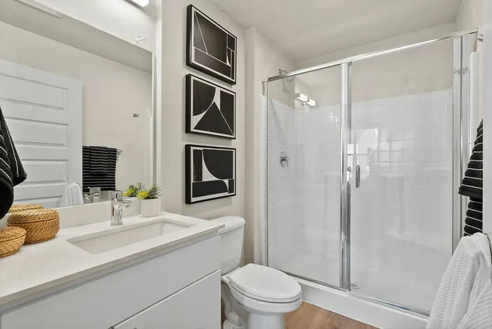 Two-Bedroom Apartments in Vancouver, WA - Bennington on First - A Bathroom with a Vanity, Sink, Mirror, Toilet, Glass-Enclosed Shower, Wall Art, and Towel Accents.