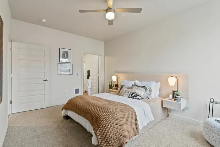 Three-Bedroom Apartments in Vancouver, WA - Bennington on First - Bedroom with Carpeted Floor, Bed, Floating Nighstands with Lamps, Ceiling Fan, and Ensuite Bathroom