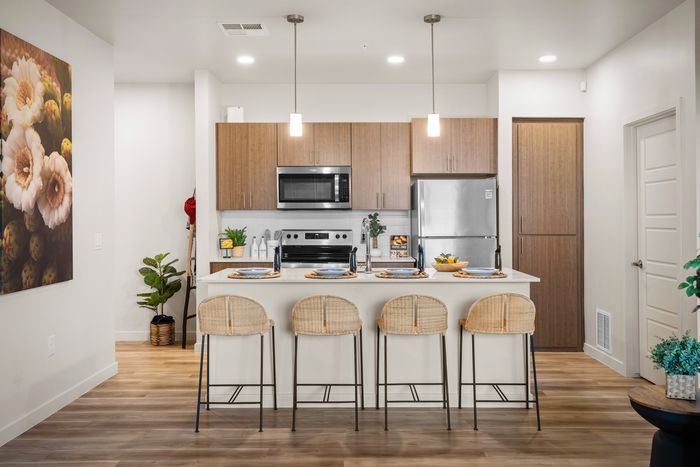 Pet-Friendly Luxury Apartments in Eastmark AZ - Acero Hawes Crossing - Modern, Bright Kitchen with Quartz Countertops, Stainless Steel Appliances, Wood-Patterned Cabinetry, Cooking Island, White Tile Backsplash, and Stool Seating