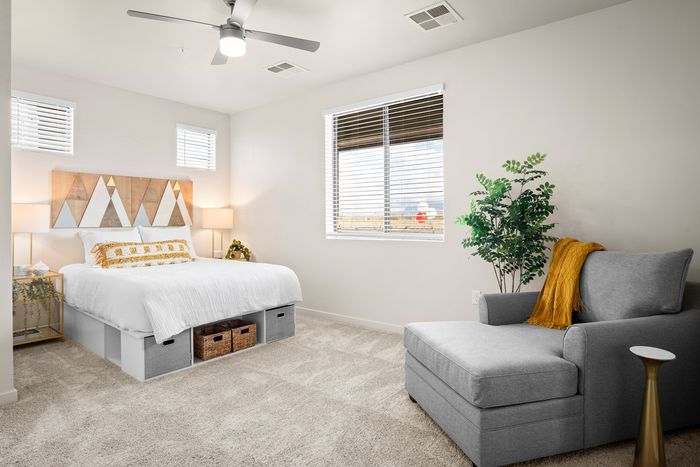 Three Bedroom Luxury Apartments in Eastmark AZ - Acero Hawes Crossing - Carpeted Bedroom with White Walls, a Ceiling Fan, a Bed, an Armchair, and Three Windows