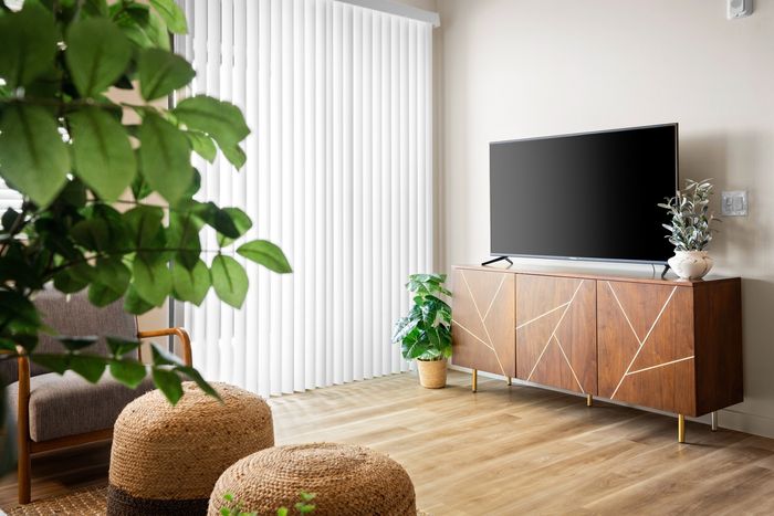 Eastmark, AZ, Pet-Friendly Luxury Apartments - Acero Hawes Crossing - Bright Living Room With Wood Style Flooring, Vertical Blinds, Mid Century Media Console, And Potted Plants.
