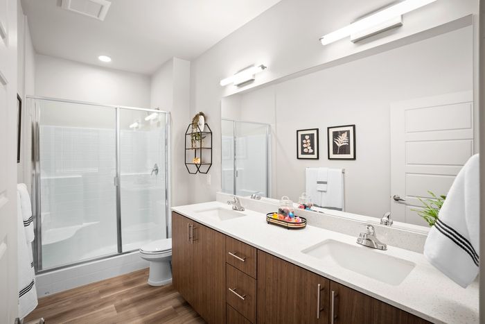 Luxury Apartments in Mesa, AZ, for Rent - Acero Hawes Crossing - Bathroom with Vinyl Plank Flooring, Double Vanity Sink with Quartz Countertops, Large Mirror, and Spacious Shower with Sliding Glass Door.