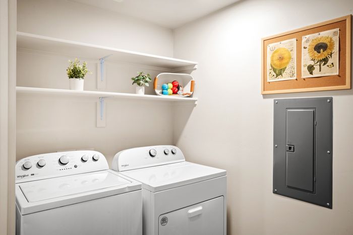 Pet-Friendly, Luxury Apartments in Eastmark, AZ - Acero Hawes Crossing - In-Home Laundry Room With Washer And Dryer, White Wall Shelving, Storage Decor, And Bright Overhead Lighting.