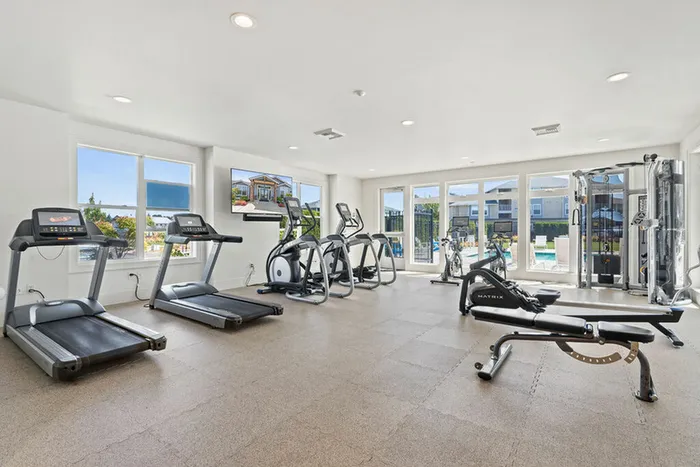Dog-Friendly Apartments In Ridgefield, WA - Acero Ridgefield - Fitness Center With A Pool View Equipped With Cardio And Weight Lifting Machines, T.V., And A Workout Bench