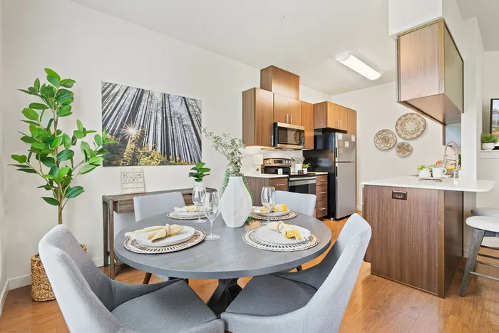 Dog-Friendly Apartments in Ridgefield, WA - Acero Ridgefield - Open Dining Area Next To Kitchen With Gray Round Table and Chairs, Wood Cabinets, Stainless Steel Appliances, and Breakfast Bar Seating.