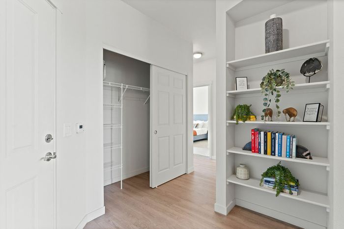 Apartments in Vancouver, WA, with In-Unit Washer and Dryer - Acero Jensen Park - A Closet Area with Built-in Shelving, Décor, Books, a Hallway Leading to a Bedroom, and Wood-Style Flooring.