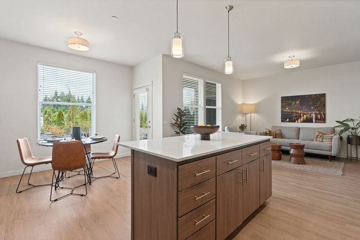 Apartments in Vancouver, WA - Acero Jensen Park - An Open-Concept Apartment Interior with a Kitchen Island, Pendant Lighting, Dining Area, Living Area, and Wood-Style Flooring.