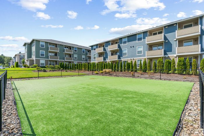 Vancouver, WA, pet Friendly Apartments - Acero Jensen Park - A Dog Park with a Fenced, Surrounding Residential Buildings, Landscaping, and Open Sky.