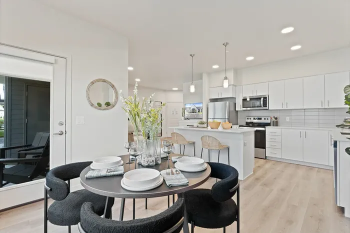 Two-Bedroom Apartments in Camas, WA - Bennington on First - Open Concept Dining Area And Kitchen Featuring A Round Dining Table With Upholstered Chairs, Wood Flooring, And Adjacent To The Kitchen.