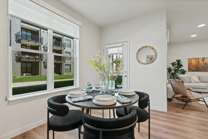 Vancouver, WA, Columbia Tech Center Apartments - Bennington on First - A Dining Area with a Round Table Set for Four, Upholstered Chairs, Table Décor, a Large Window, Wood-Style Flooring.