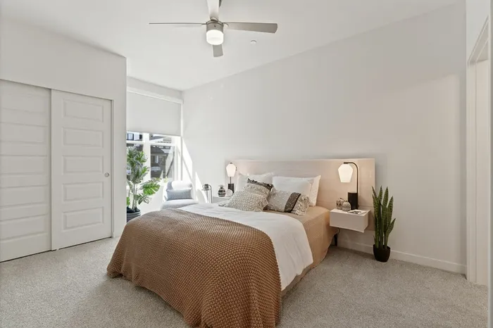 Three-Bedroom Apartments in Camas, WA - Bennington on First - Bright Bedroom With Upholstered Bed, Neutral Bedding, Ceiling Fan, Nightstands With Modern Lamps, And Large Window Seating Nook.