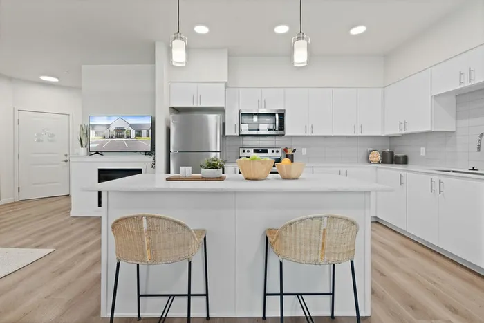 3-Bedroom Apartments in Camas, WA - Bennington on First - Spacious White Kitchen With Oversized Quartz Island, Pendant Lights, Stainless Steel Appliances, And Wood Style Flooring.