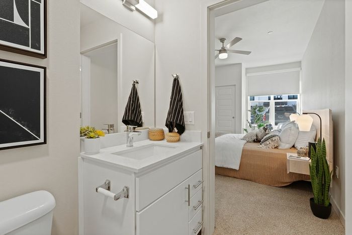 Three-Bedroom Apartments in Vancouver, WA - Bennington on First - Bedroom with Carpeted Floor, Bed, Floating Nighstands with Lamps, Ceiling Fan, and Ensuite Bathroom