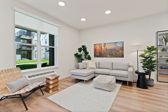 2-Bedroom Apartments in Vancouver, WA - Bennington on First - A Contemporary Living Room with a Sectional Sofa, Accent Chair, Area Rug, Side Table, and Indoor Plants.