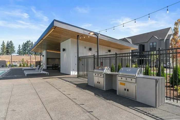 Vancouver, WA, Apartments for Rent - Bennington on First - A Grilling Area with Built-in Grills, Covered Pavilion, Lounge Seating, String Lights, and Fencing.