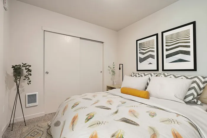Inviting bedroom with cozy feather-themed bedding, chic geometric artwork, and a sleek potted plant for a serene ambiance.