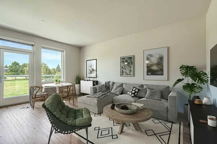 Inviting living room with a cozy gray sectional sofa, stylish decor, and bright natural light from large windows overlooking a lush green yard.