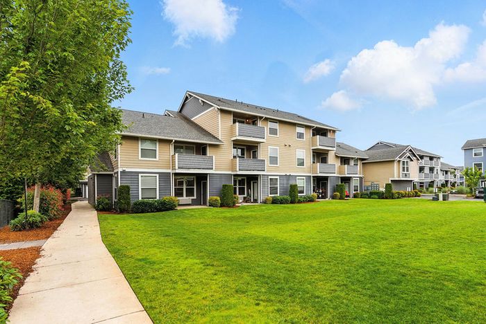 Charming modern apartment complex with landscaped grounds, featuring spacious balconies against a clear blue sky.