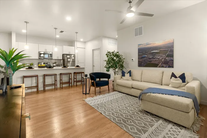 3-Bedroom Apartments in Glendale, AZ - Acero at the Stadium - Open-Concept Living Room With Wood Style Floors, L-Shaped Couch, Armchair, Wall Art, and Modern Ceiling Fan.