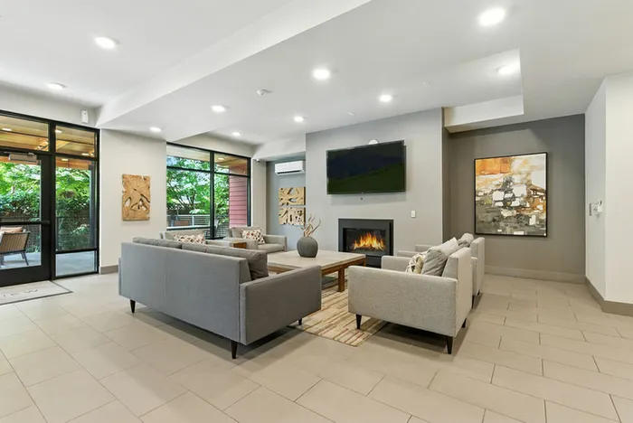 Modern living room with stylish gray sofas, a cozy fireplace, and large windows offering natural light and greenery views.