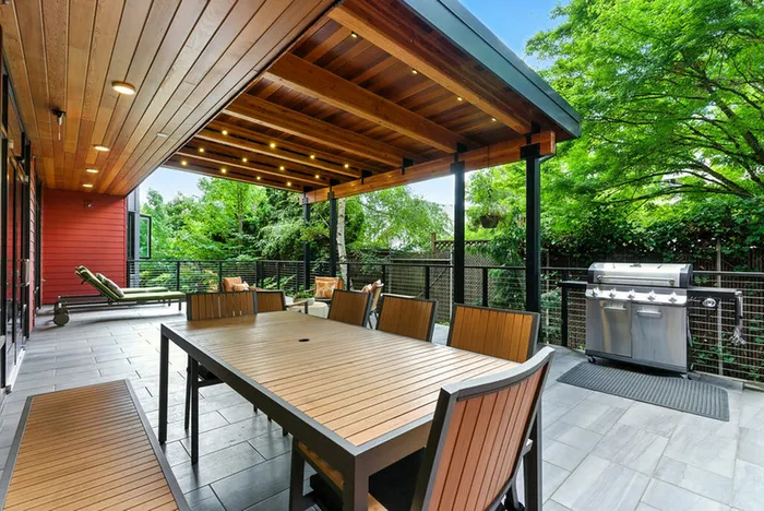 Elegant outdoor patio with a wooden ceiling, modern dining set, and a sleek grill surrounded by lush greenery.