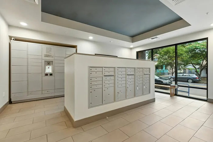 Modern apartment mailroom featuring secure parcel lockers and individual mailboxes with a sleek, stylish design and large windows for natural light.