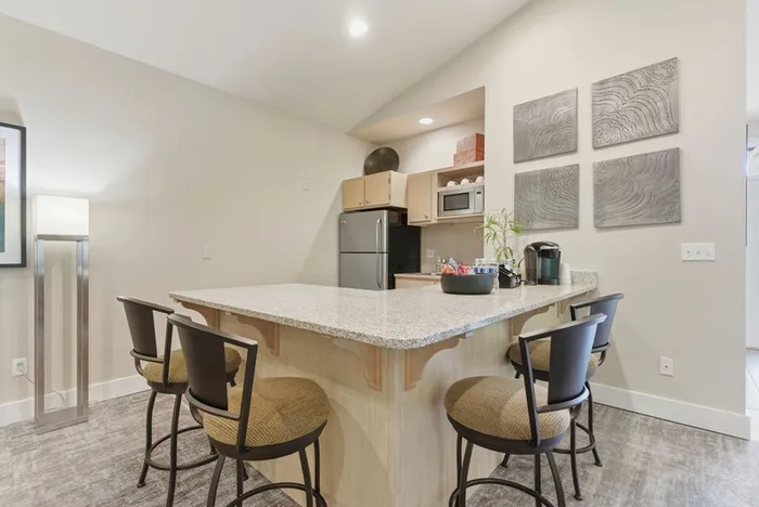 Modern kitchen with a stylish island, sleek countertops, cozy chairs, and contemporary wall art, designed for comfort and elegance.