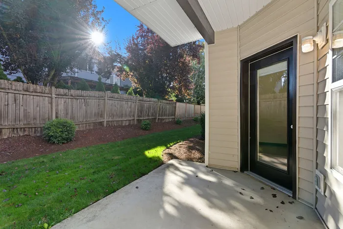 Charming patio view from a cozy apartment, featuring a sunlit garden space with lush greenery and a stylish sliding door.