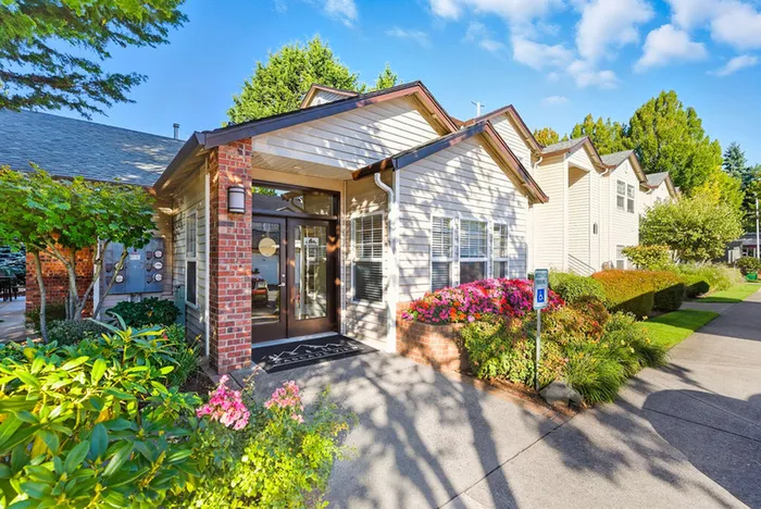 Charming apartment exterior with lush landscaping and vibrant flowers, nestled in a serene, sunny neighborhood.